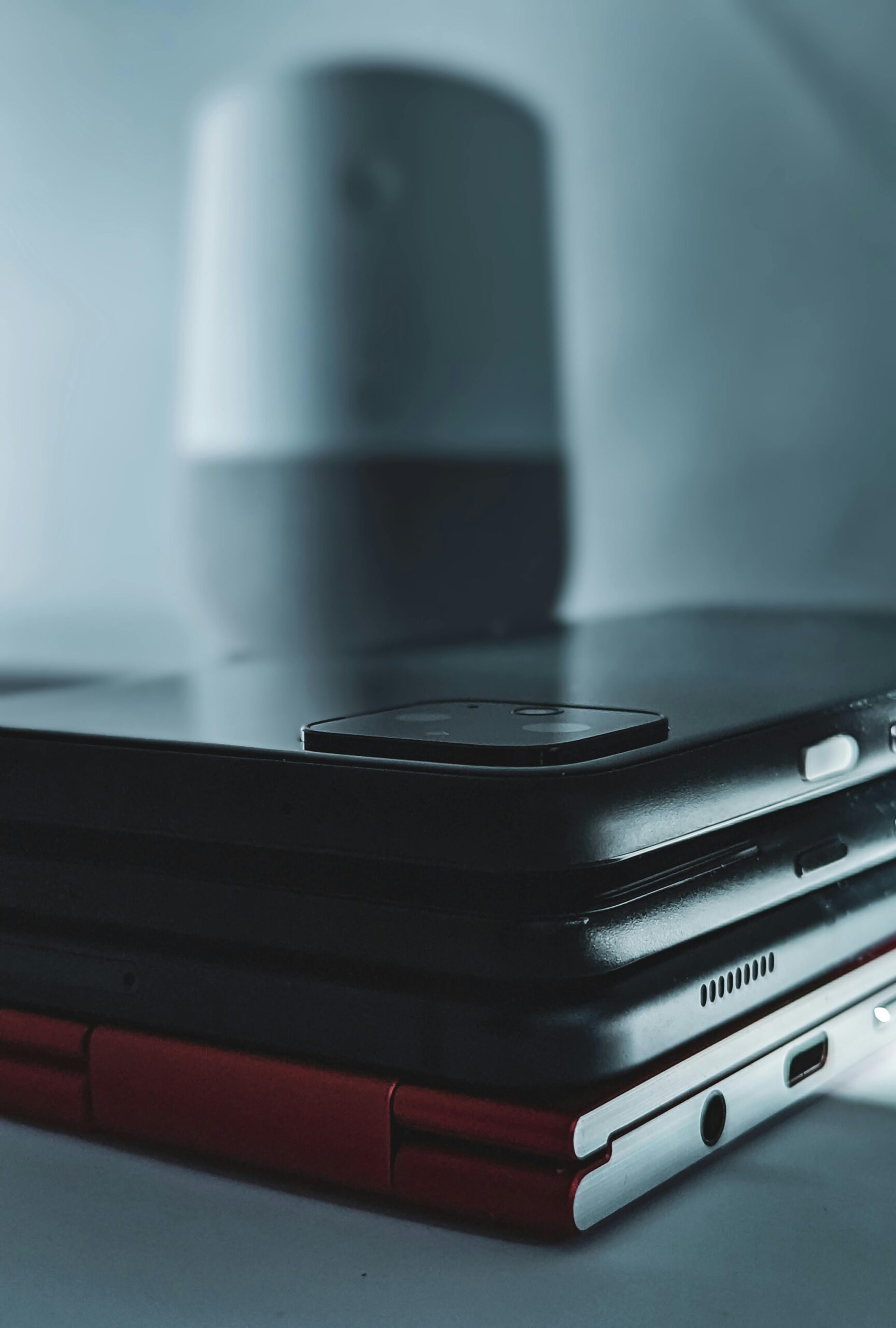 Close-up of stacked modern devices including smartphones and a tablet with wireless speaker in background.